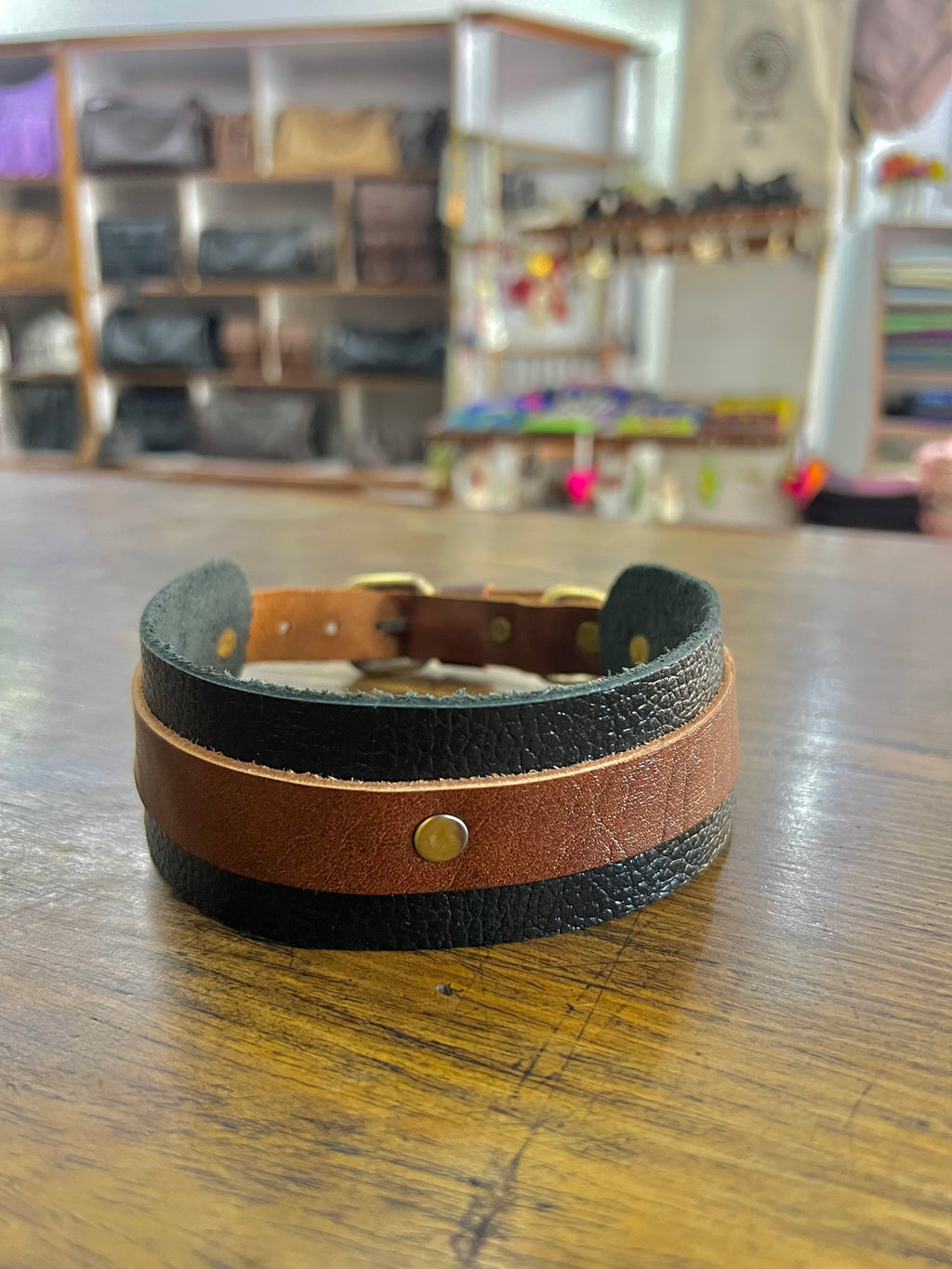 Brown and black leather dog collar on a wooden surface with a blurred background